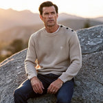 Man draagt een ecru Faguo trui, zittend op een rots in een natuurlijke omgeving